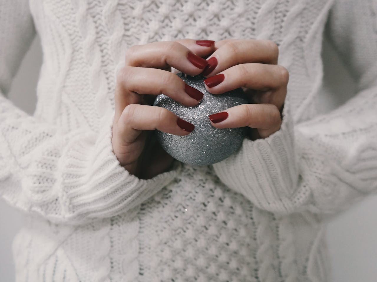 Home Hands with red manicure holding a silver glitter ball, perfect for winter holiday themes.