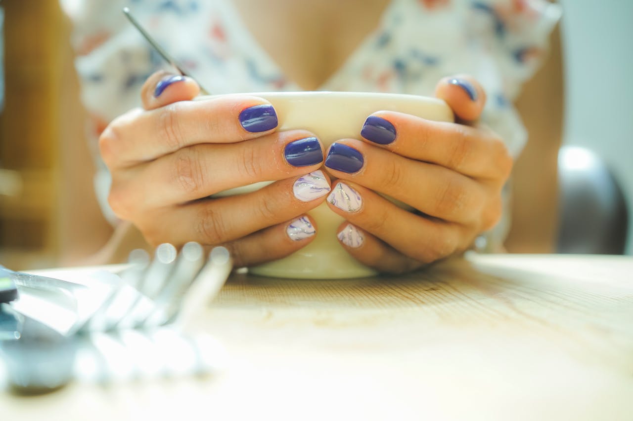 Home A woman with colorful nails holds a mug, capturing a moment of warmth and style indoors.