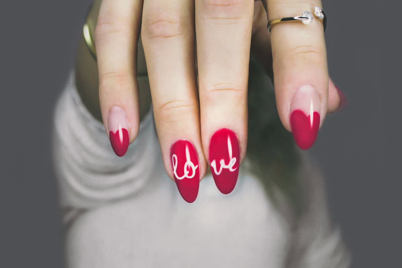 Home Vibrant red nails with love art on a womans hand, showcasing elegant style and design.
