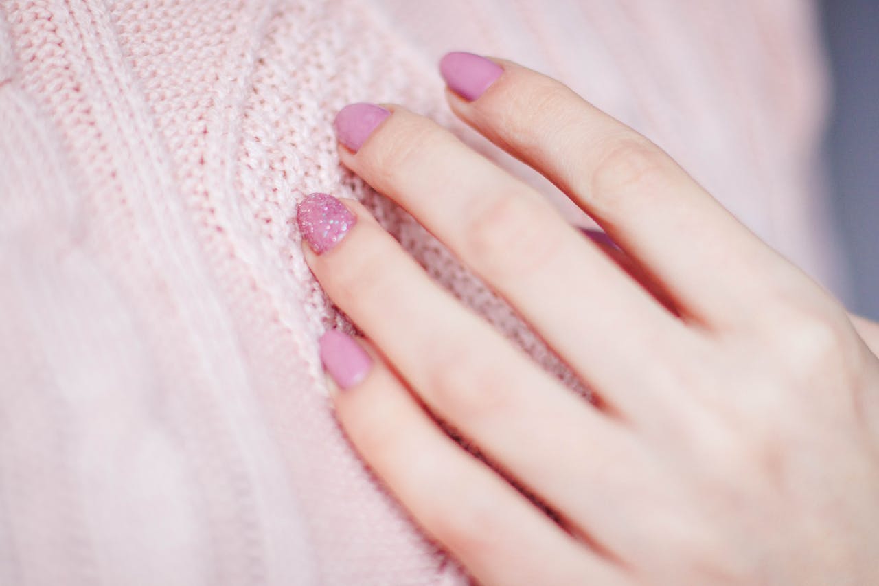 Home Close-up of a womans hand with pink manicure resting on a soft knit sweater, showcasing elegance and fashion.
